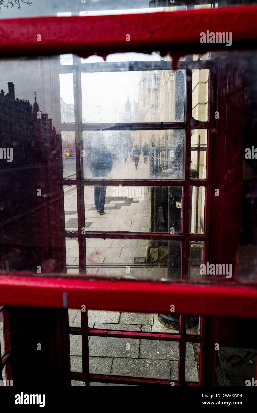 strada cittadina con i pedoni visti attraverso una vecchia cabina telefonica Foto Stock