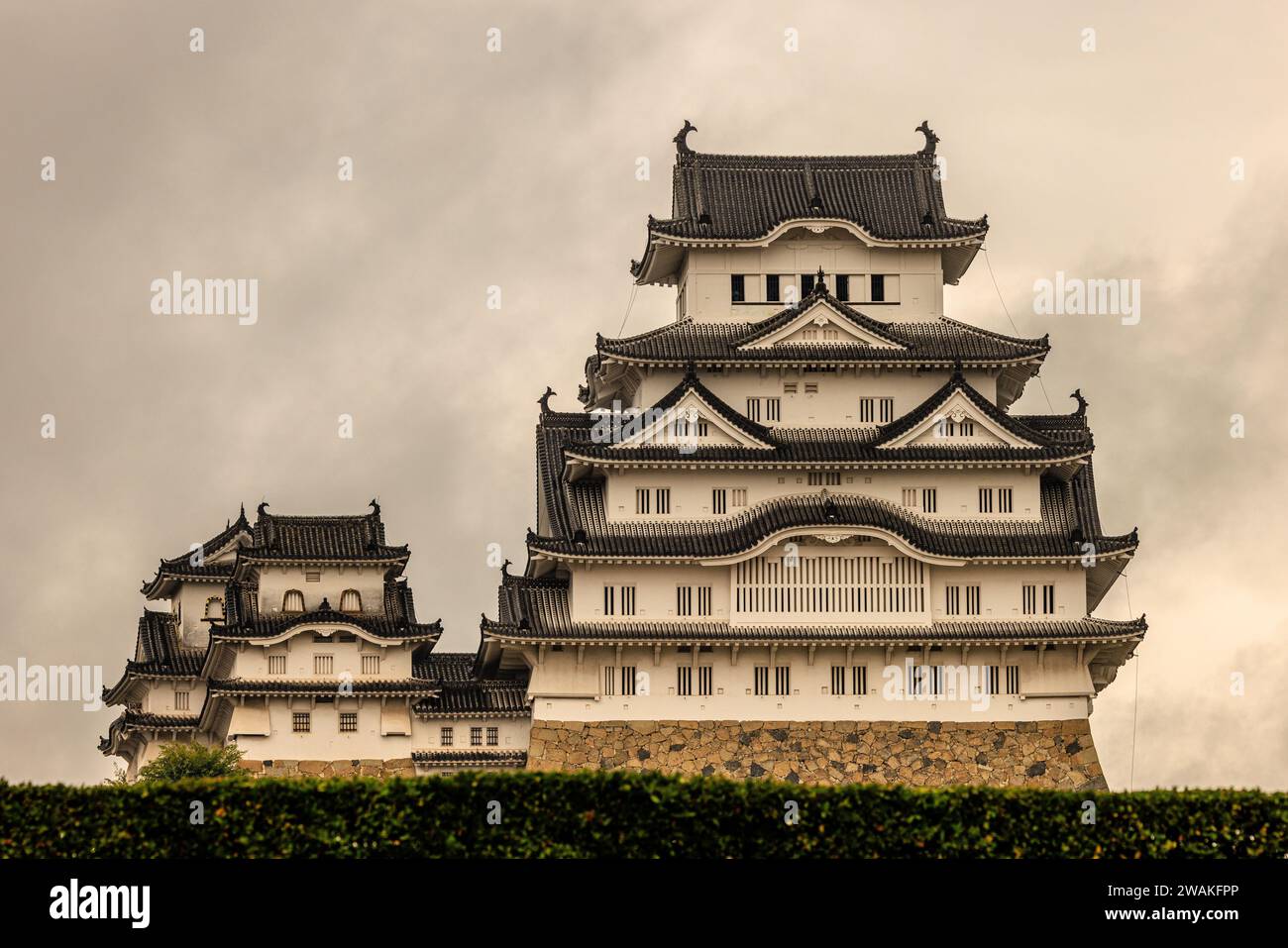 vista frontale del castello di himeji che guarda verso l'alto alla facciata bianca e a più piani sotto un cielo scuro che minaccia un temporale Foto Stock