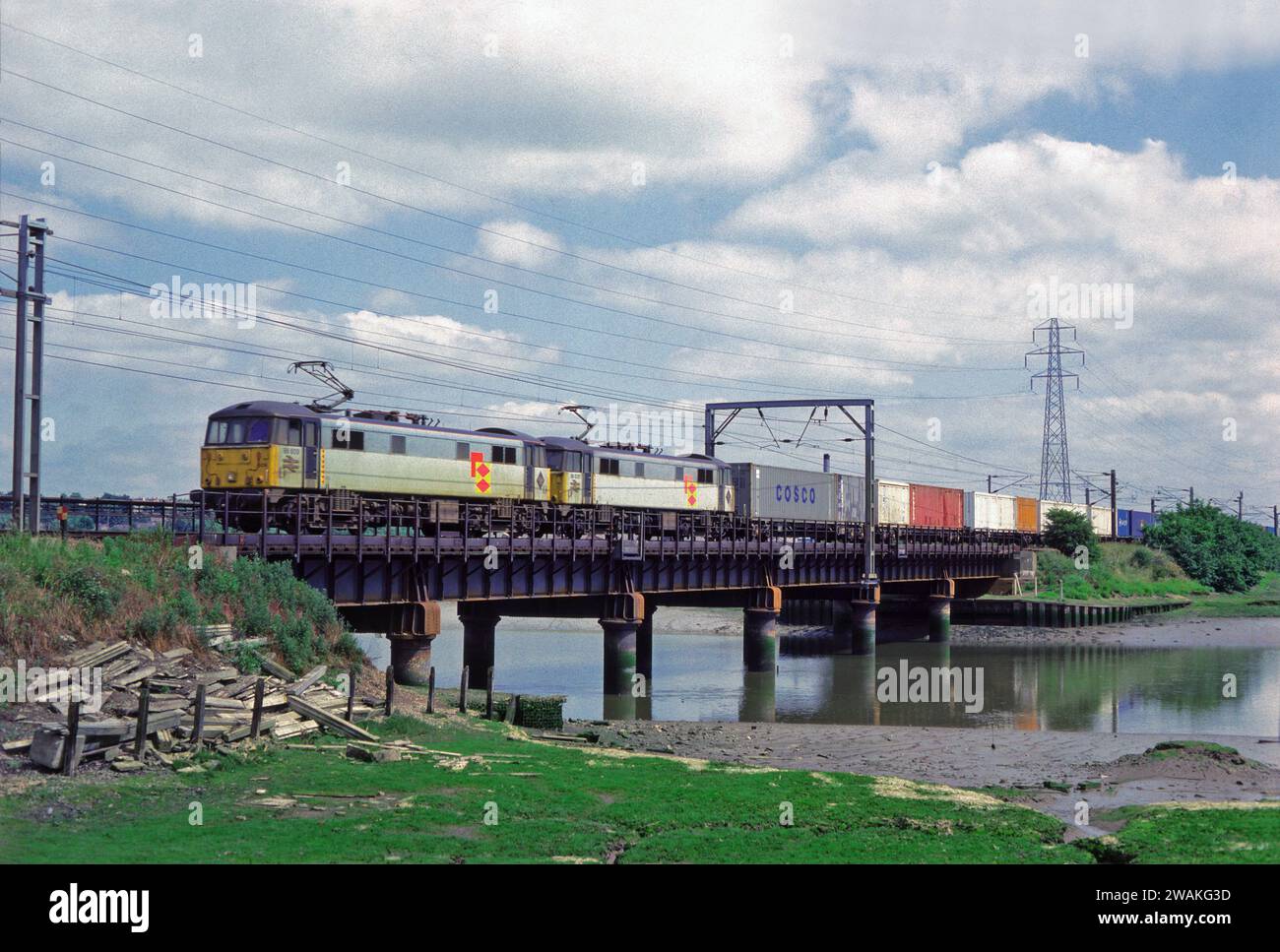 Un paio di locomotive elettriche di classe 86, numeri 86609 e 86635, che lavoravano su un freightliner ben carico che attraversava il fiume Stour a Manningtree il 15 giugno 1993. Foto Stock Un paio di locomotive elettriche di classe 86, numeri 86609 e 86635, che lavoravano su un freightliner ben carico che attraversava il fiume Stour a Manningtree il 15 giugno 1993. Foto Stock