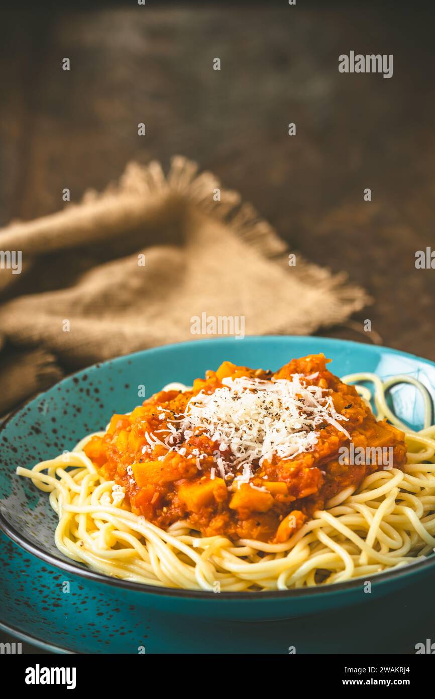 Spaghetti con salsa alla bolognese vegan fatta in casa a base di lenticchie rosse e zucca su fondo di legno, terracotta turchese, verticale con spazio copia Foto Stock