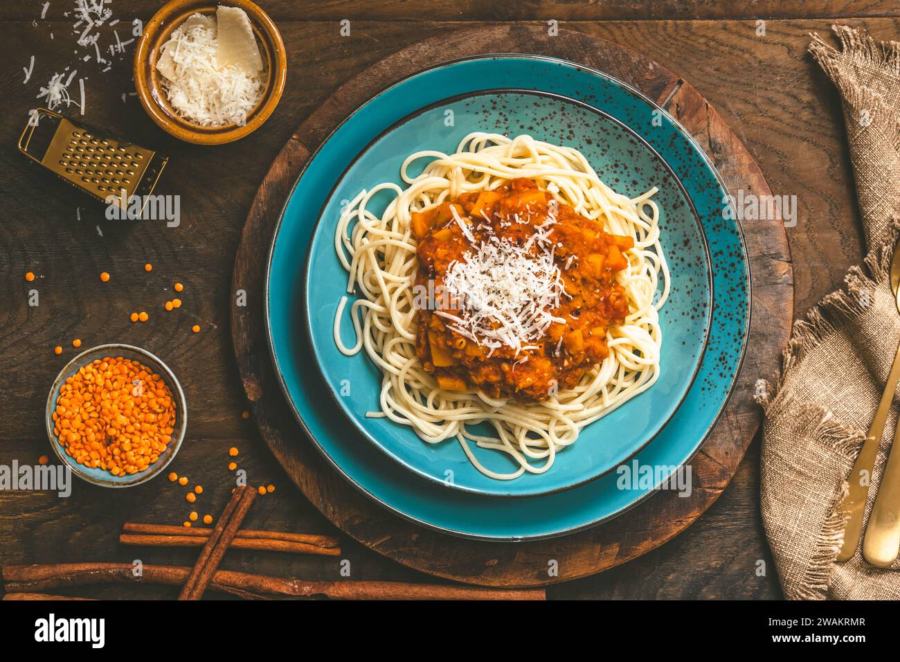 Spaghetti con salsa vegan alla bolognese fatta in casa a base di lenticchie rosse e zucca su fondo di legno, terracotta turchese, vista dall'alto Foto Stock