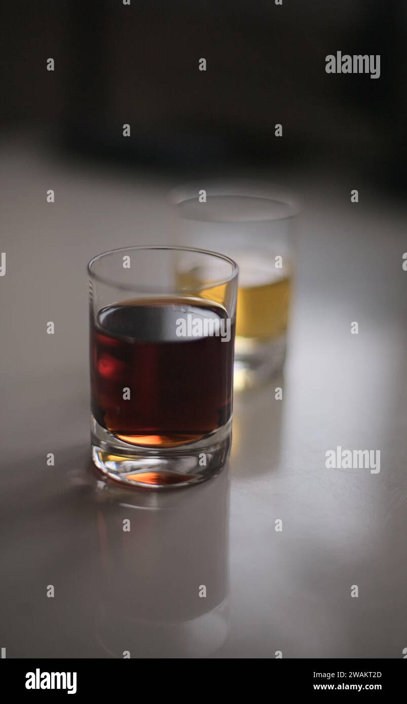Due bicchieri da shot ripieni di bevande alcoliche rosse e gialle retroilluminate su un tavolo bianco lucido Foto Stock