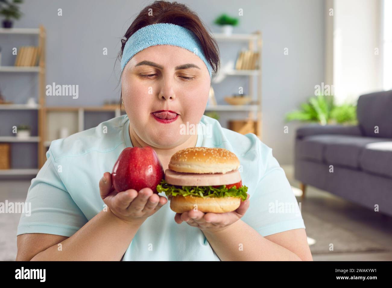 Donna grassa divertente con mela e hamburger cercando di fare la scelta tra cibo sano e malsano Foto Stock