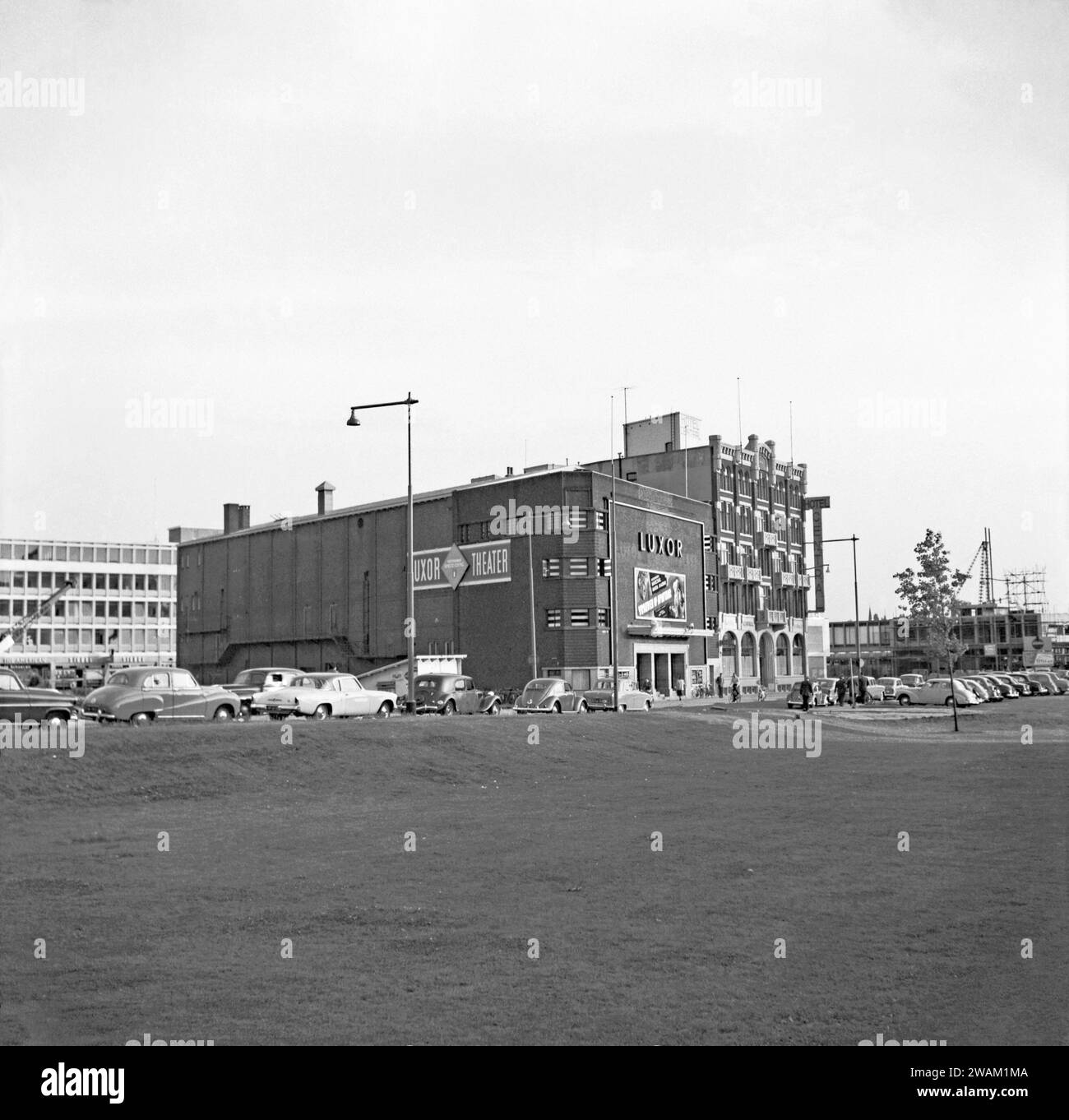 Una veduta di Rotterdam nel 1955 – questa è stata fotografata guardando attraverso un'area erbosa fino alle auto parcheggiate su Kruikade e al teatro Old Luxor – la proiezione è stata "Vrouwen op Avontuur" con Georges Marchal e Maria Mauban. Accanto all'hotel si trova l'Hotel Centraal. L'area ha subito danni da bombe durante la seconda guerra mondiale e questa visione è ora passata con moderni edifici alti che sostituiscono aree aperte come questa, una fotografia d'epoca degli anni '1950. Foto Stock