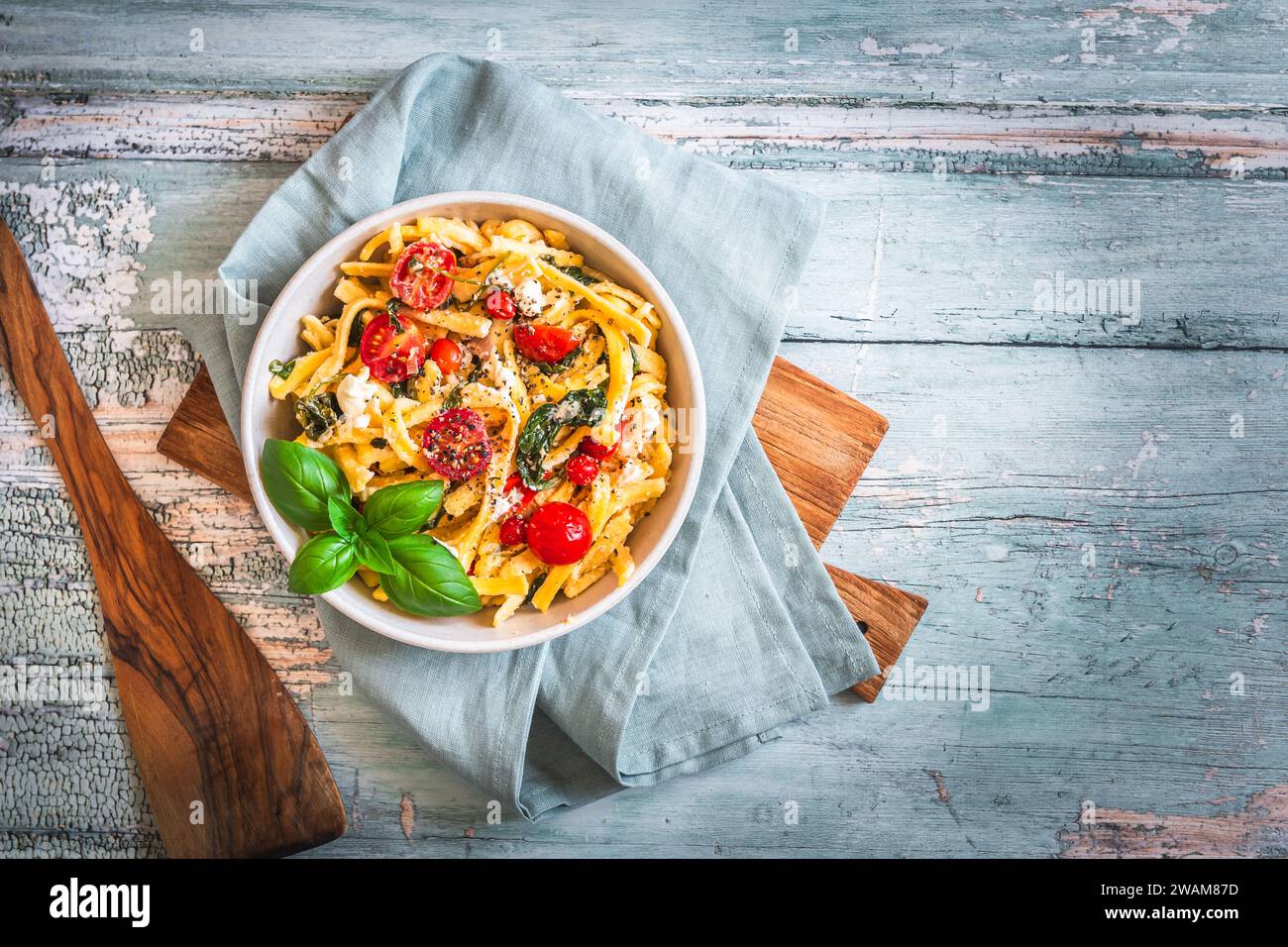 Ciotola di pasta, spaghetti, spaetzle sveve, con spinaci e pomodori ciliegini su un tavolo rustico in legno, vista dall'alto Foto Stock