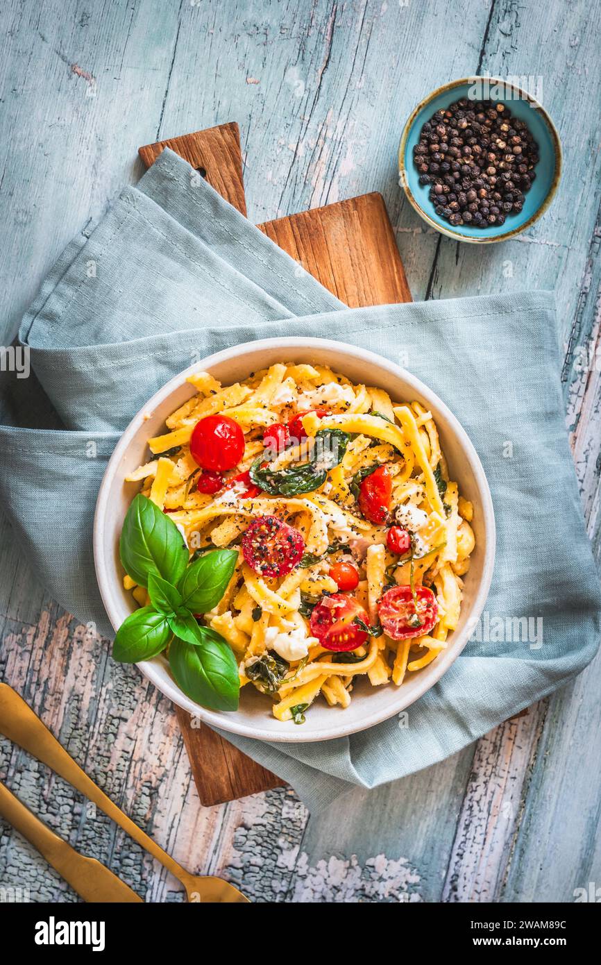Ciotola di pasta, spaghetti, spaetzle sveve, con spinaci e pomodori ciliegini su un tavolo rustico in legno, vista dall'alto Foto Stock