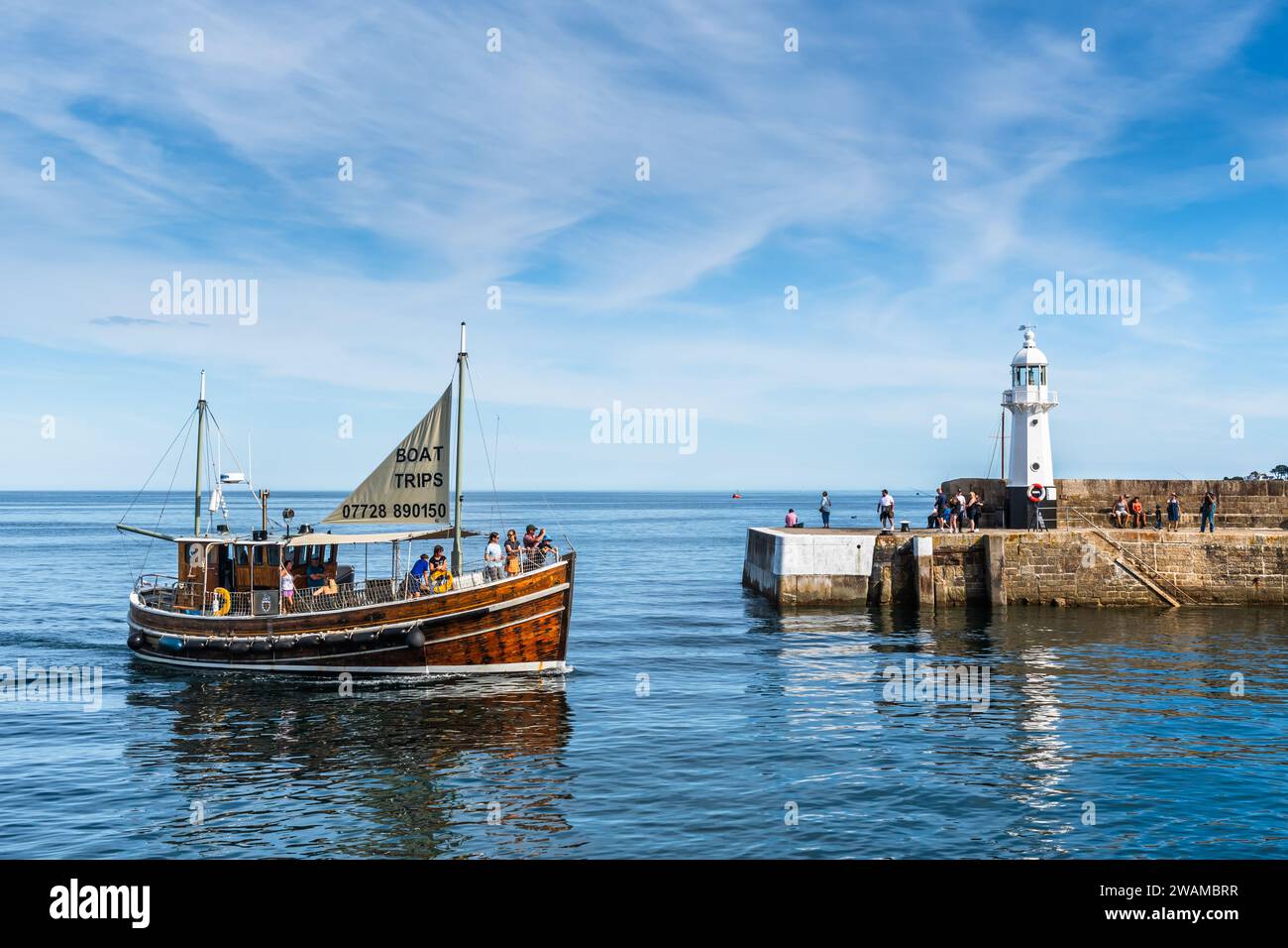 Mevagissey, Cornovaglia, Regno Unito - 16 agosto 2023: Il faro e l'ingresso al porto di Mevagissey sulla costa meridionale della Cornovaglia. Sta arrivando una barca turistica Foto Stock