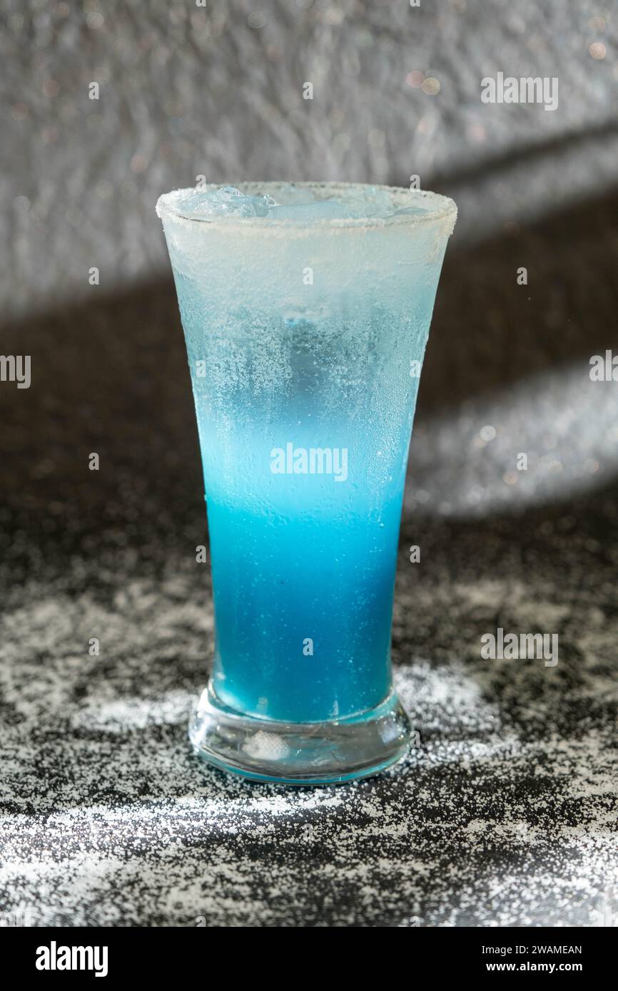 Un primo piano di un vetro riempito di liquido blu posizionato su una superficie bianca del piano di lavoro Foto Stock