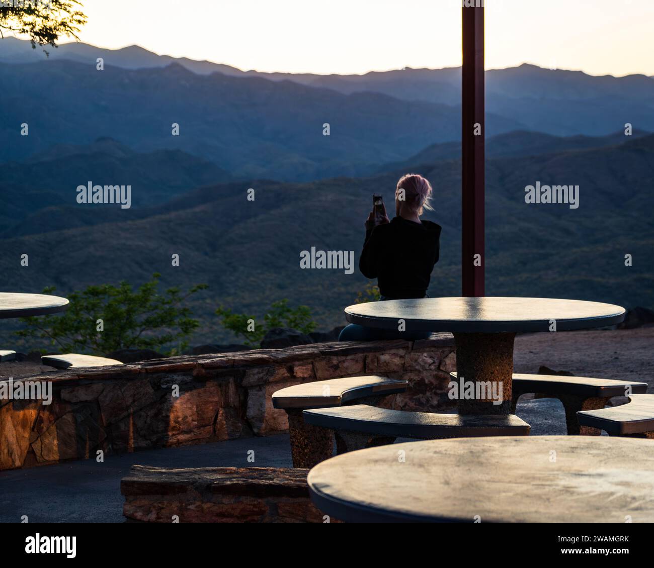 Vista posteriore di una donna bionda che usa un cellulare per fotografare le montagne al Sunset Point Rest Stop in Arizona, Stati Uniti. Foto Stock