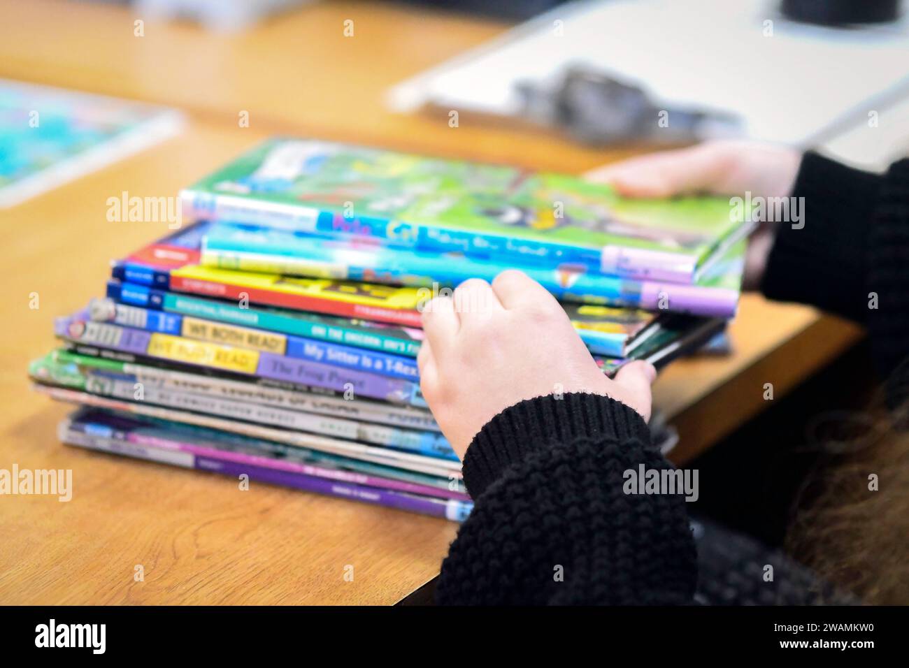 Immagine delle mani di una bibliotecaria mentre sfreccia tra una pila di libri per bambini che sono fuori fuoco. I libri per bambini sono stati al centro dei divieti di libri AC Foto Stock