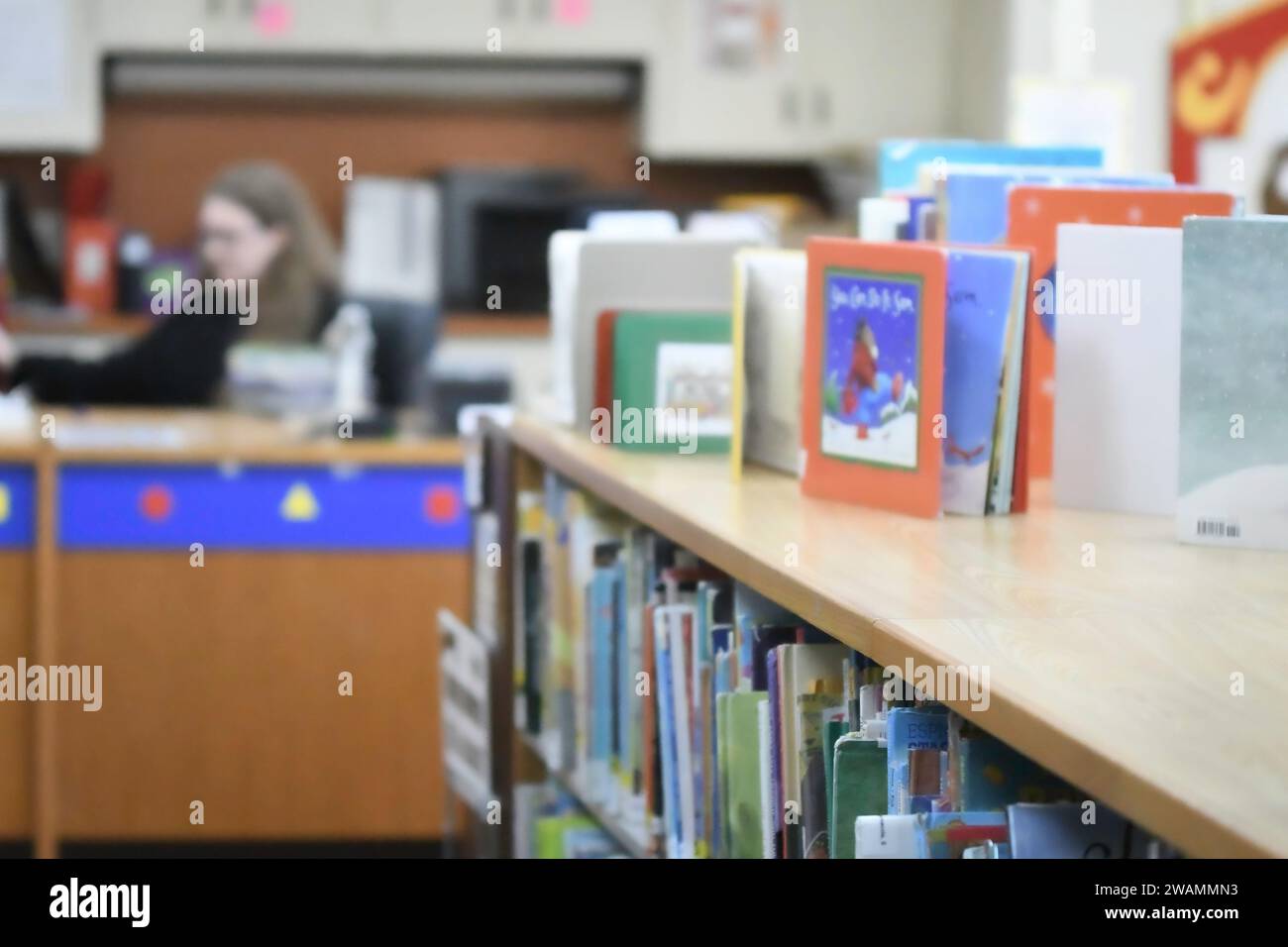 Libri per bambini sfocati in una biblioteca con bibliotecaria sfocata sullo sfondo. Foto Stock