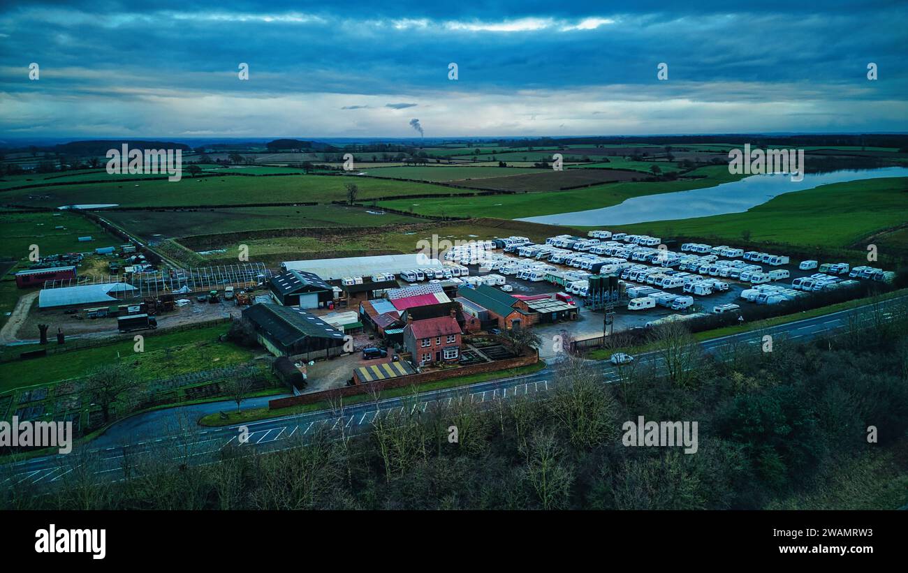 Vista aerea di un paesaggio rurale con terreni agricoli, un fiume e edifici raggruppati sotto un cielo nuvoloso al crepuscolo. Foto Stock