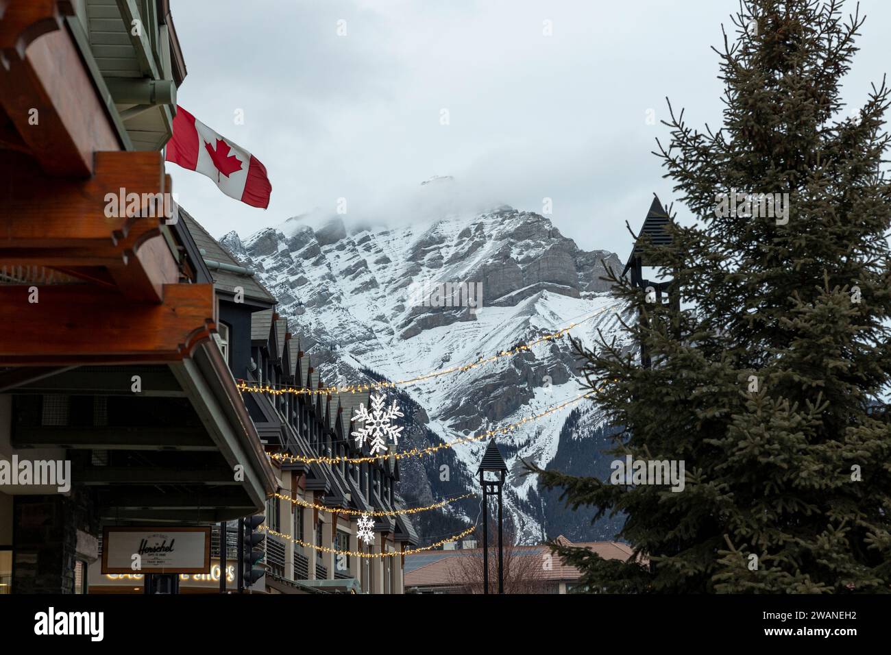 Banff, Alberta, Canada. Guardando a nord lungo Banff Avenue, nei negozi, nelle luci di Natale e Cascade Mountain nel tardo pomeriggio invernale. Foto Stock