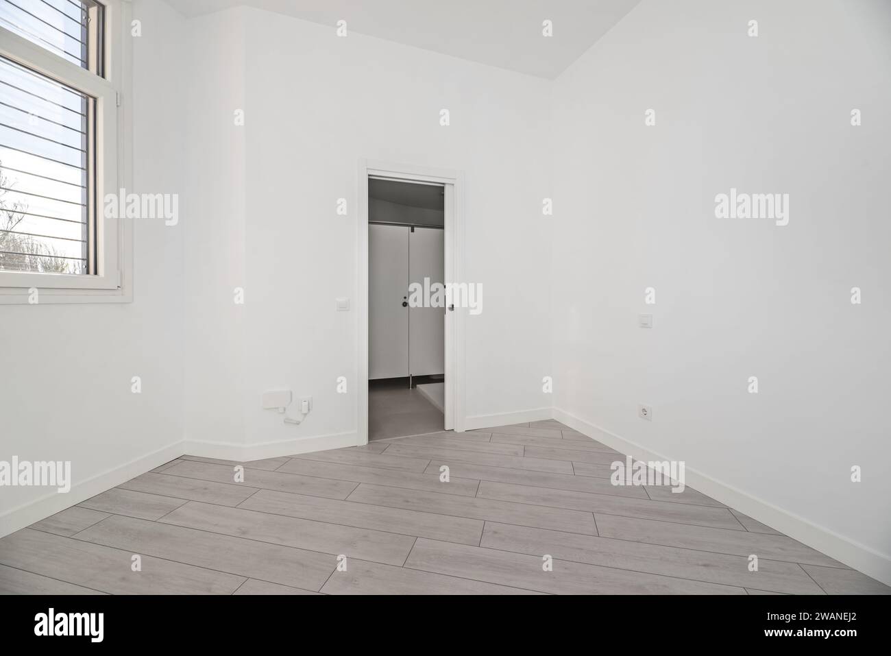 Una camera vuota in una casa al piano terra con pavimenti in parquet grigio, pareti dipinte di bianco semplice e accesso ad un bagno recentemente installato. Foto Stock