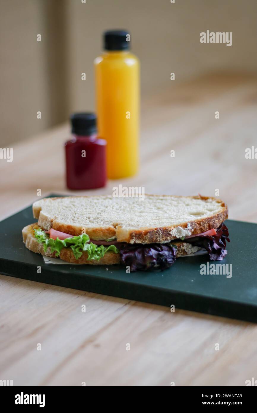 Hamburger con lattuga e formaggio su tagliere di legno con bottiglia di succo sul tavolo Foto Stock