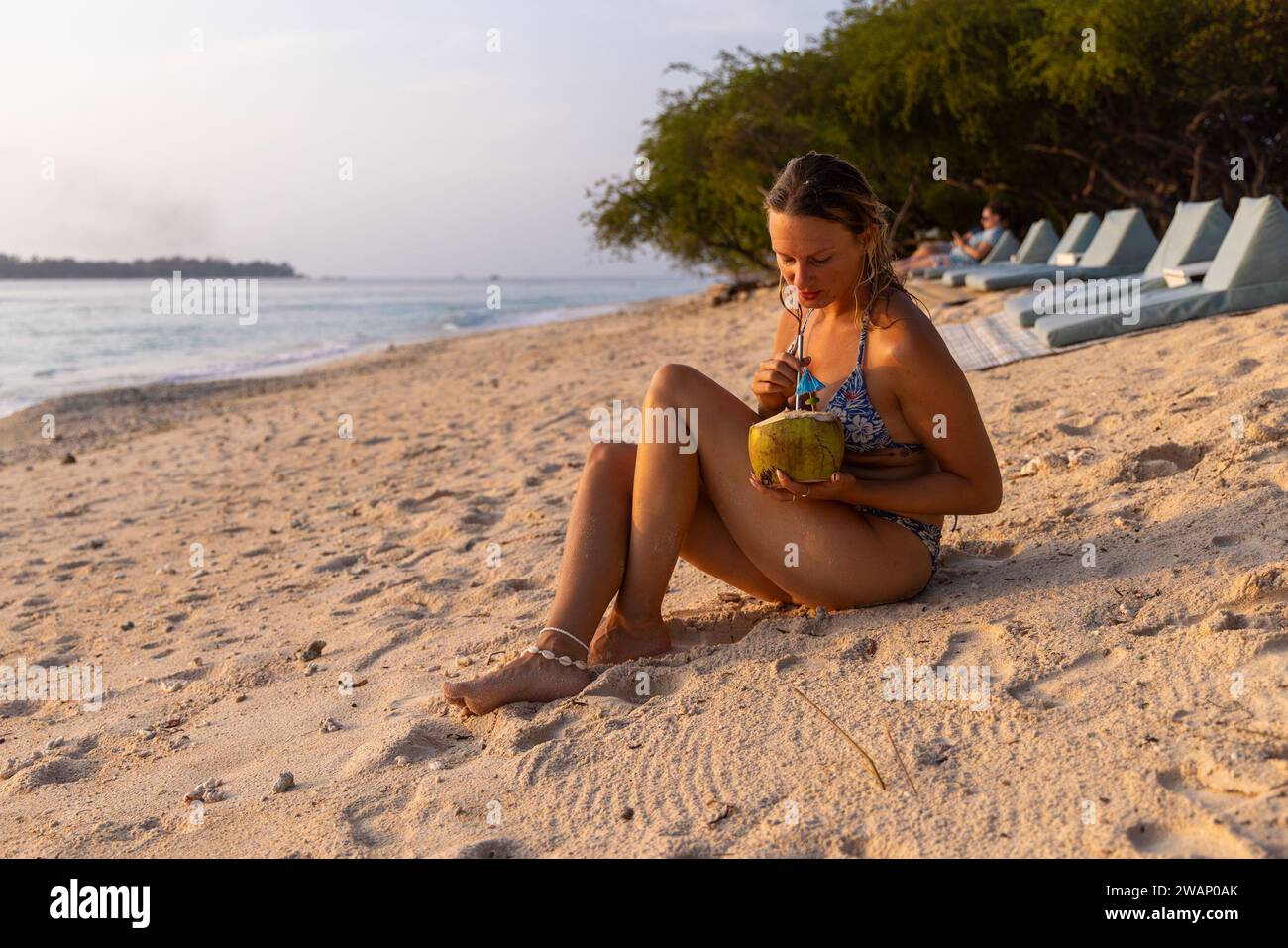 Una giovane donna sta bevendo l'acqua di cocco sulla spiaggia di gili meno, Indonesia Foto Stock