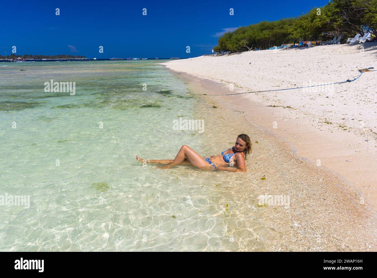Una giovane donna in costume da bagno si trova nel mare poco profondo di una spiaggia di sabbia a Gili meno, Indonesia Foto Stock