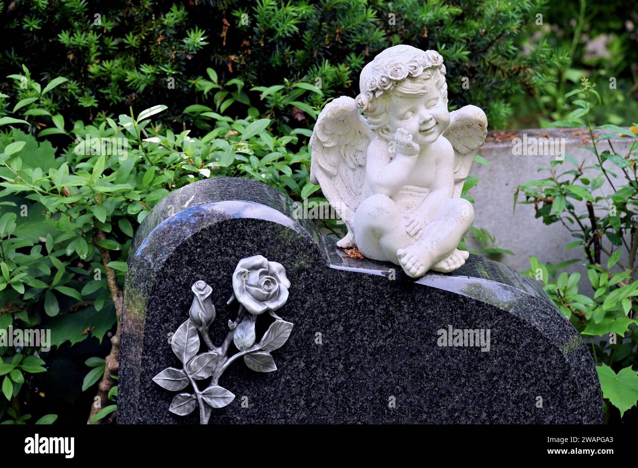 L'angelo bianco della tomba si trova su una pietra tombale nera con una rosa di pietra Foto Stock