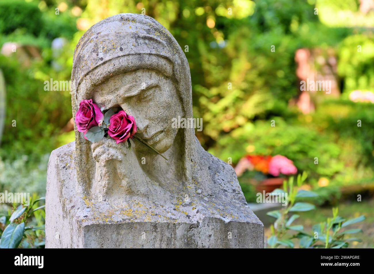 La statua in lutto con le mani e i fiori di preghiera davanti alle tombe Foto Stock
