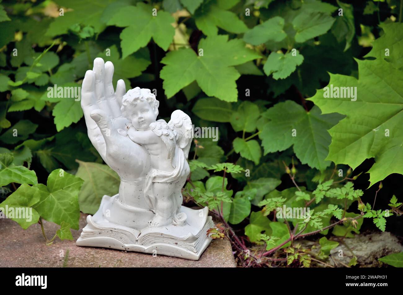 Decorazione a tombe con una mano bianca e un angelo davanti alle foglie verdi Foto Stock