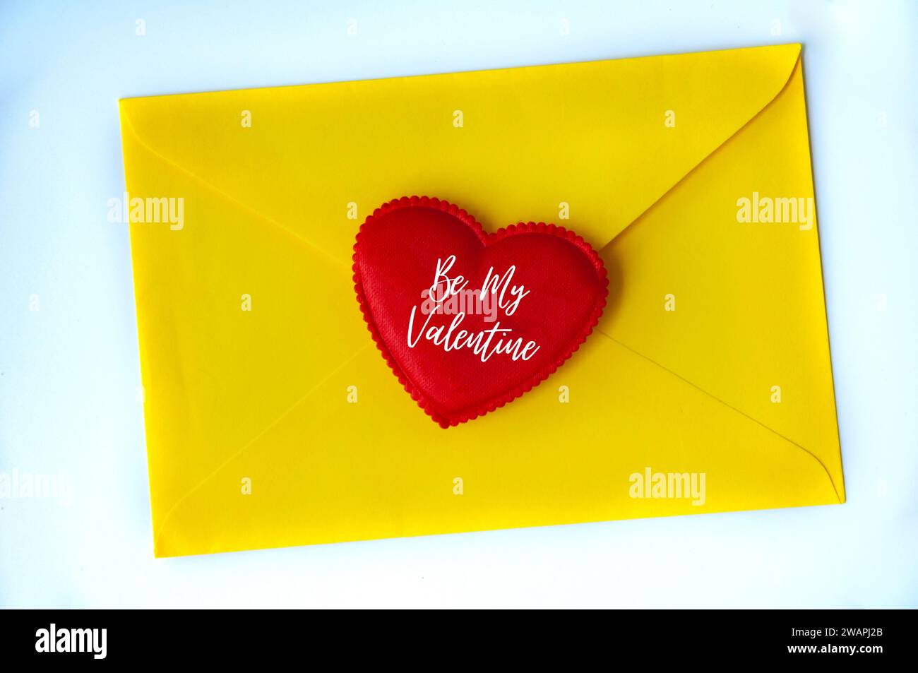 Sii il mio testo di San Valentino sulla forma del cuore su una busta di carta gialla. Concetto d'amore. Foto Stock