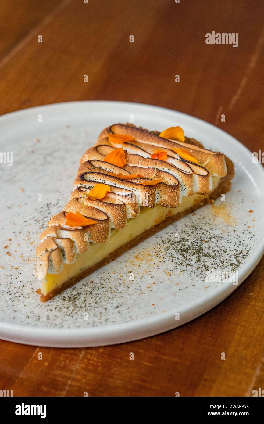 Scatto verticale di una fetta di cheesecake al limone con panna montata e petali di fiori decorativi Foto Stock