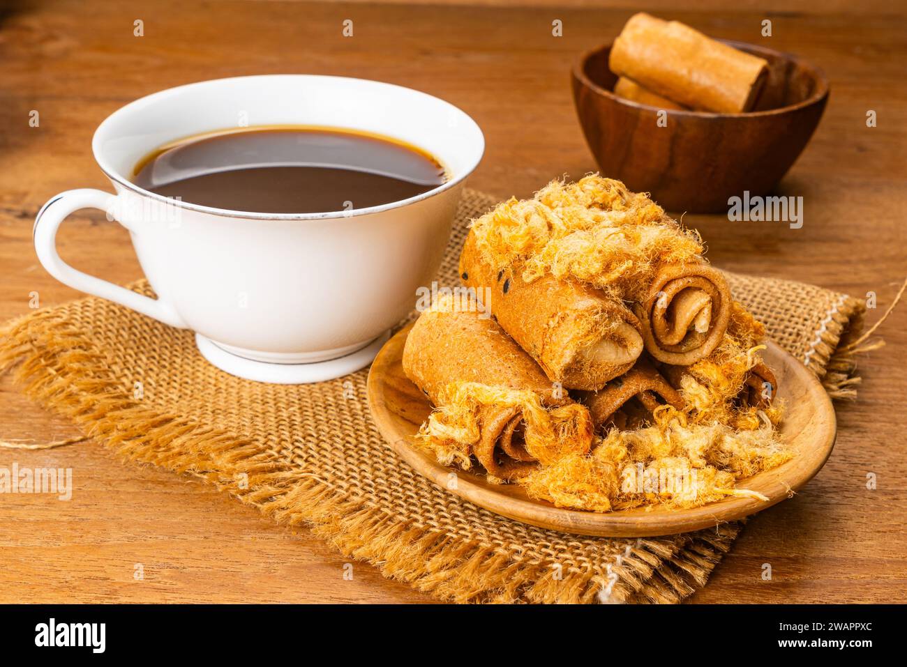 Alta pila di dolci croccanti panini di cocco con maiale scrodato essiccato in un piatto di legno con una tazza di caffè nero caldo su un sacco di telo di legno Foto Stock