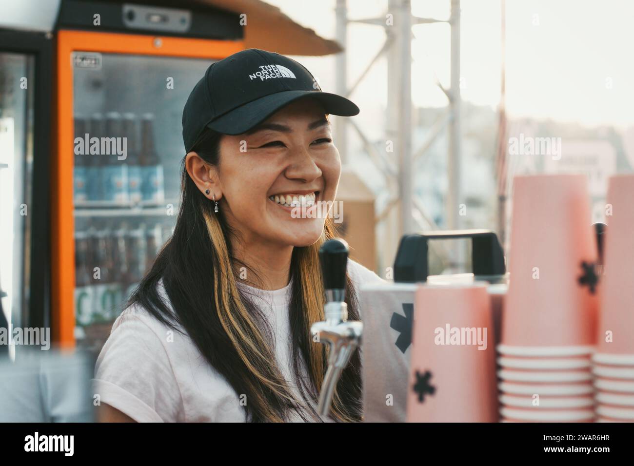 Una simpatica ragazza asiatica che lavora dietro il bancone in un bar all'aperto che vende birra Foto Stock