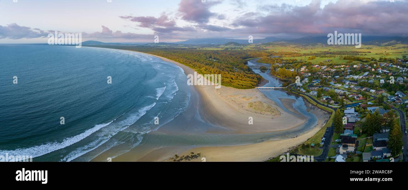 Vista aerea di una pittoresca spiaggia con sabbia bianca, acqua acquamarina e case sul lungomare annidate tra la costa Foto Stock