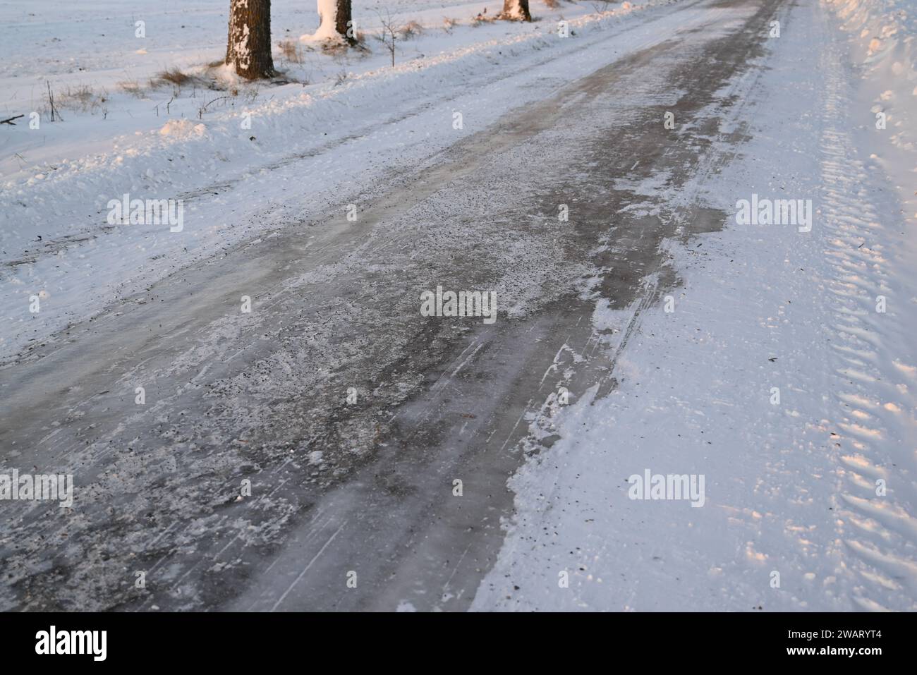 Strada ghiacciata in campagna, con segni di ghiaia e graffi da spazzaneve. Foto Stock