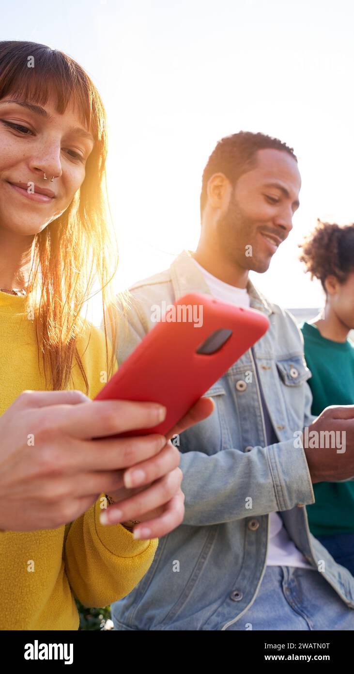 Gruppo multiculturale di amici sorridenti che utilizzano telefoni cellulari all'aperto. Persone e dipendenza tecnologica Foto Stock