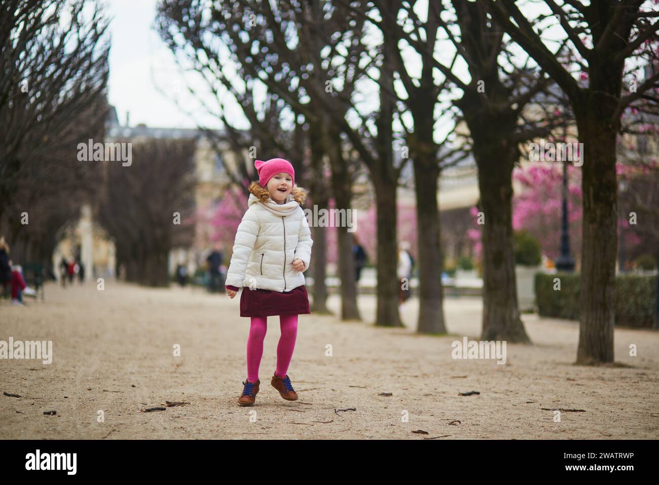 Allegra bambina in età prescolare che si diverte in una strada di Parigi, Francia all'inizio della primavera, con magnolie rosa in fiore Foto Stock