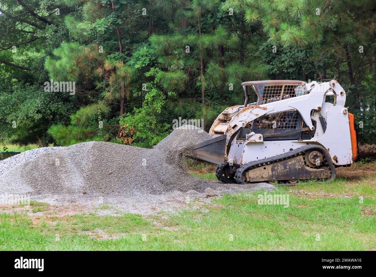 Durante la costruzione, la minipala bobcat sposta la benna contenente ghiaia in pietra frantumata Foto Stock