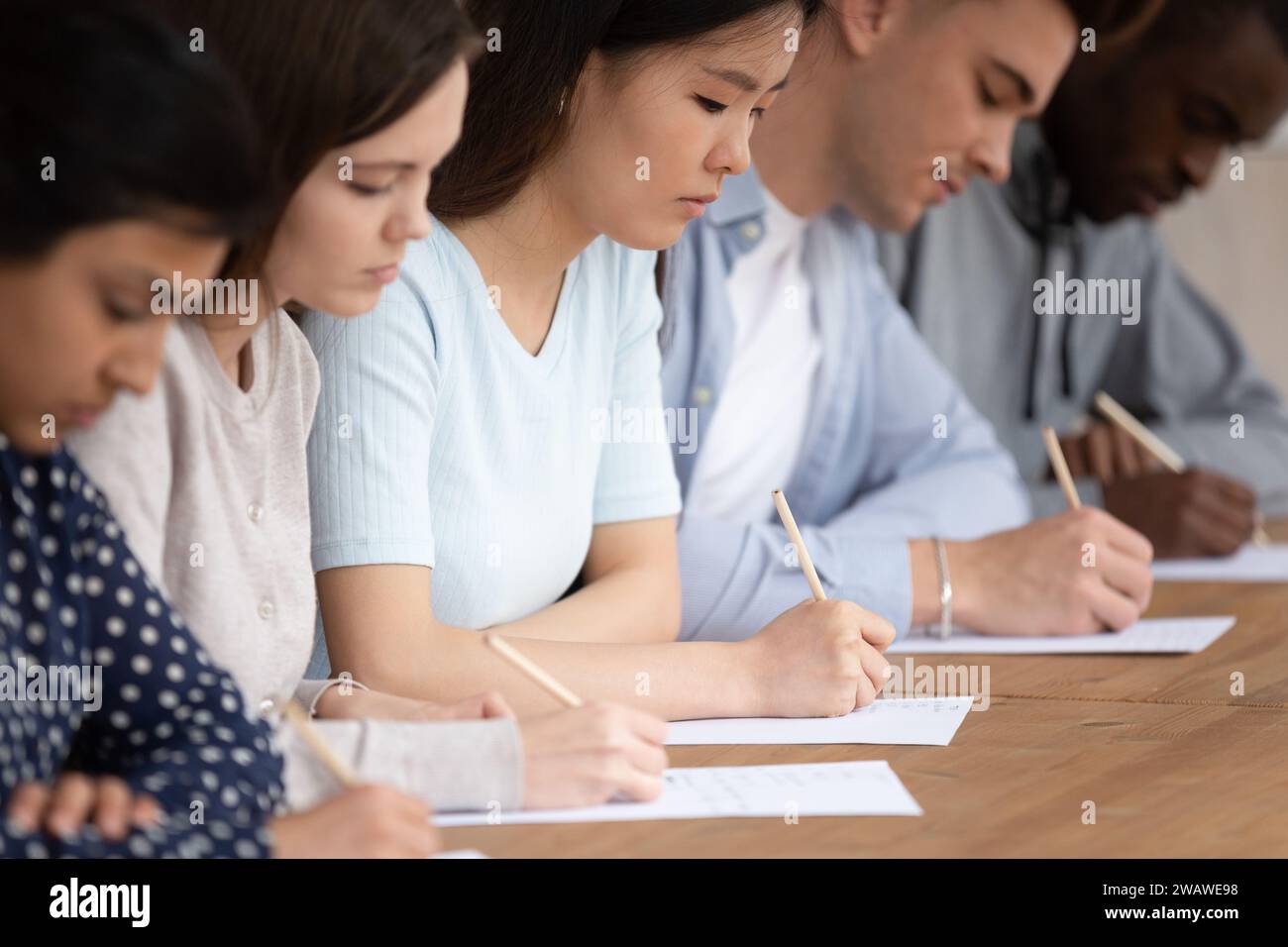 Studenti multirazziali di fila che scrivono un esame su carta Foto Stock