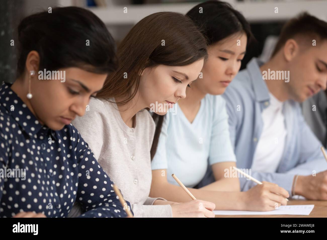 Studenti multietnici concentrati impegnati a scrivere test in classe Foto Stock
