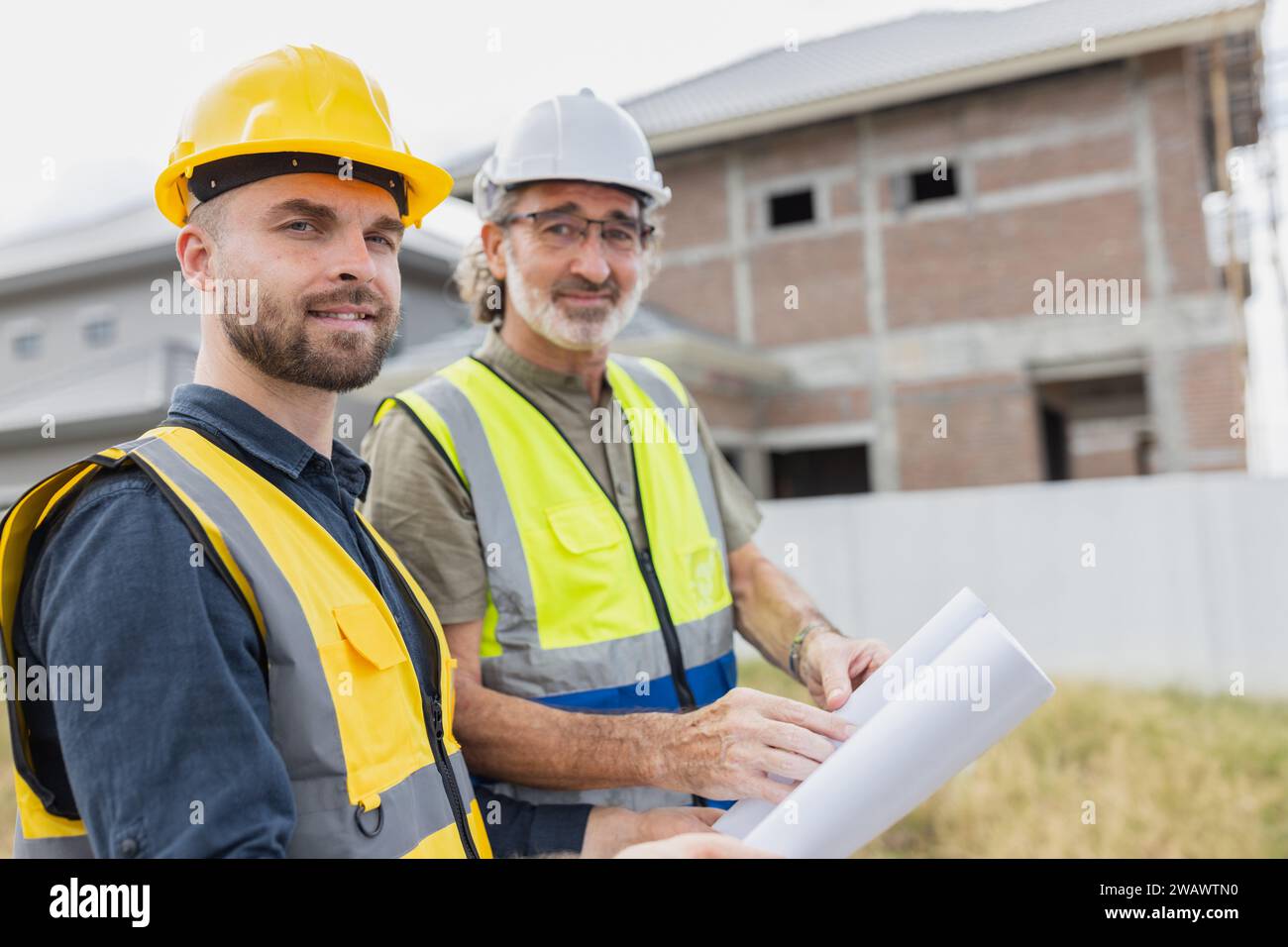 Giovane lavoratore ingegnere edile maschio che lavora collabora con il supervisore senior del progetto nel cantiere buon sorriso. Foto Stock