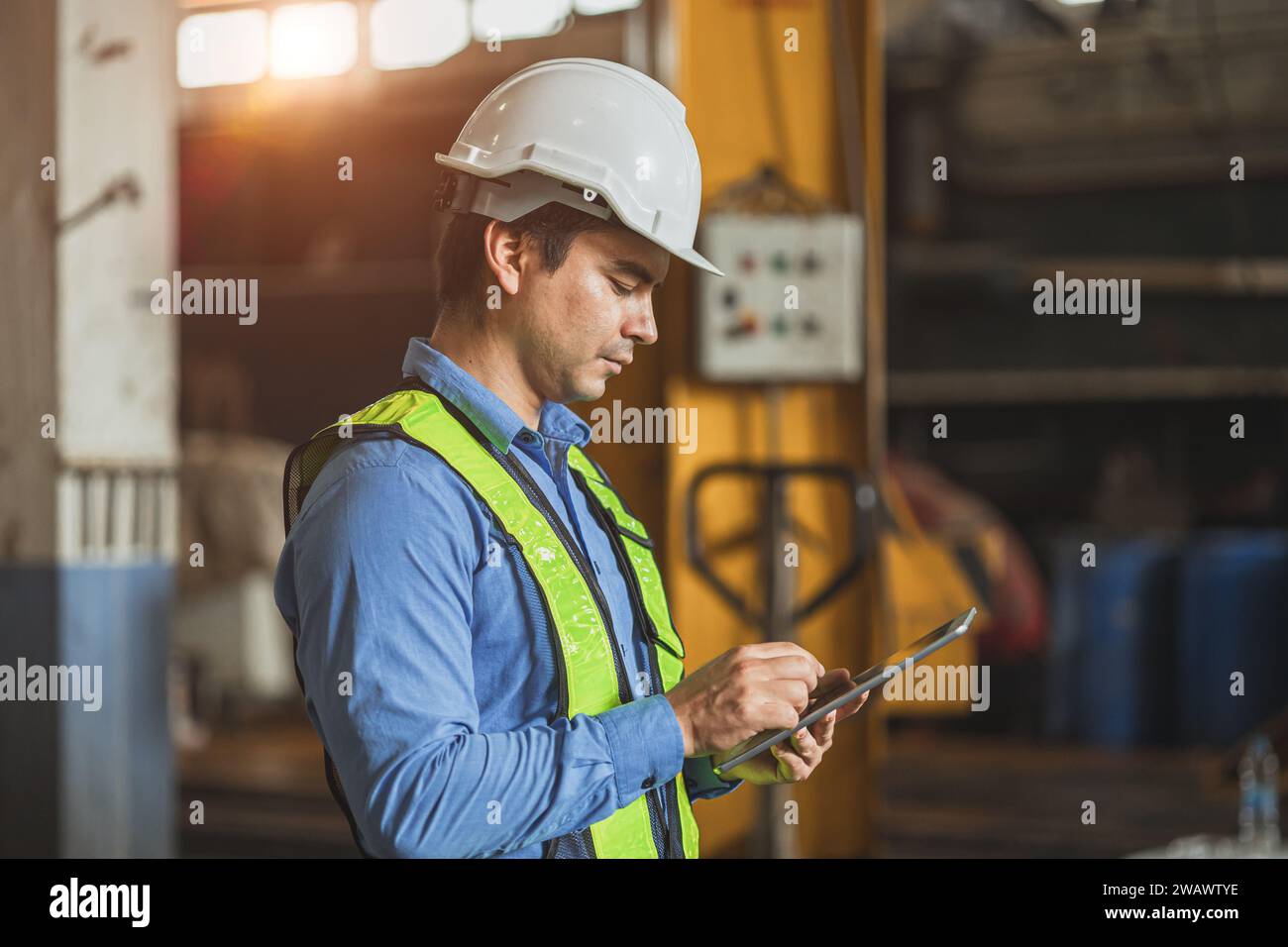 professionista adulto ingegnere senior uomo ufficiale in uniforme di sicurezza che guarda lo schermo di un tablet in officina industriale. Foto Stock