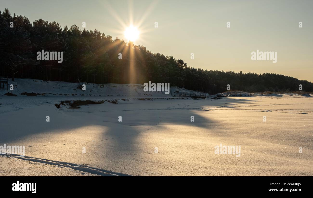 Un sentiero ricoperto di neve si illumina delicatamente nell'abbraccio della serata d'oro invernale Foto Stock