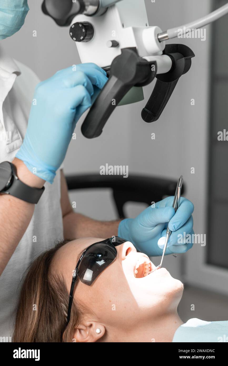 Appassionato della sua professione, il dentista nel suo ufficio utilizza un microscopio per identificare e trattare con precisione i problemi dentali. Ogni momento è un tocco Foto Stock