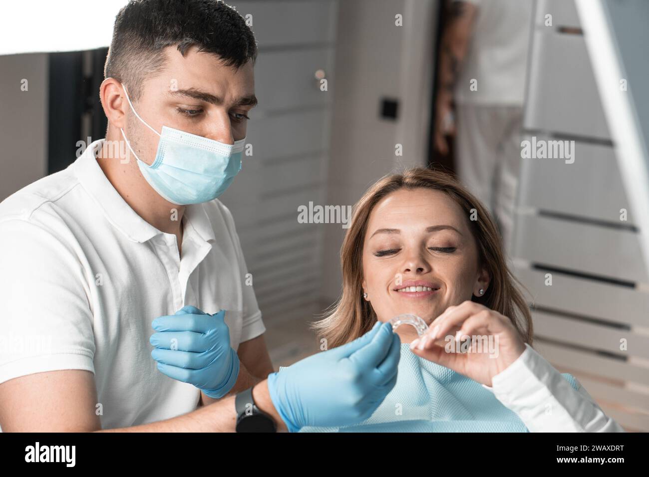 Il dentista tiene l'allineatore nelle mani, preparandosi per il trattamento di una fase importante e fornendo comfort al paziente. Spiega e dimostra i vantaggi Foto Stock