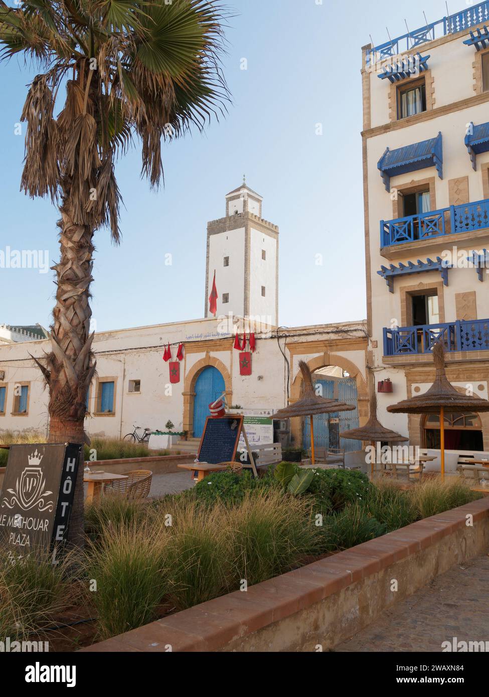 Hotel e ristorante con balconi e porte blu e giardino accanto a una torre nella storica medina nella città di Essaouira, Marocco. 7 gennaio 2024 Foto Stock
