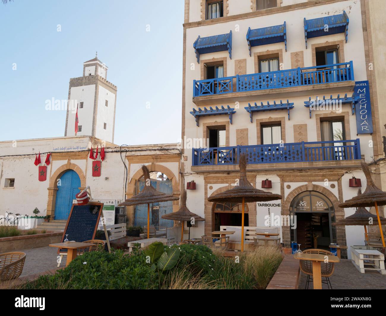 Hotel e ristorante con balconi e porte blu e giardino accanto a una torre nella storica medina nella città di Essaouira, Marocco. 7 gennaio 2024 Foto Stock