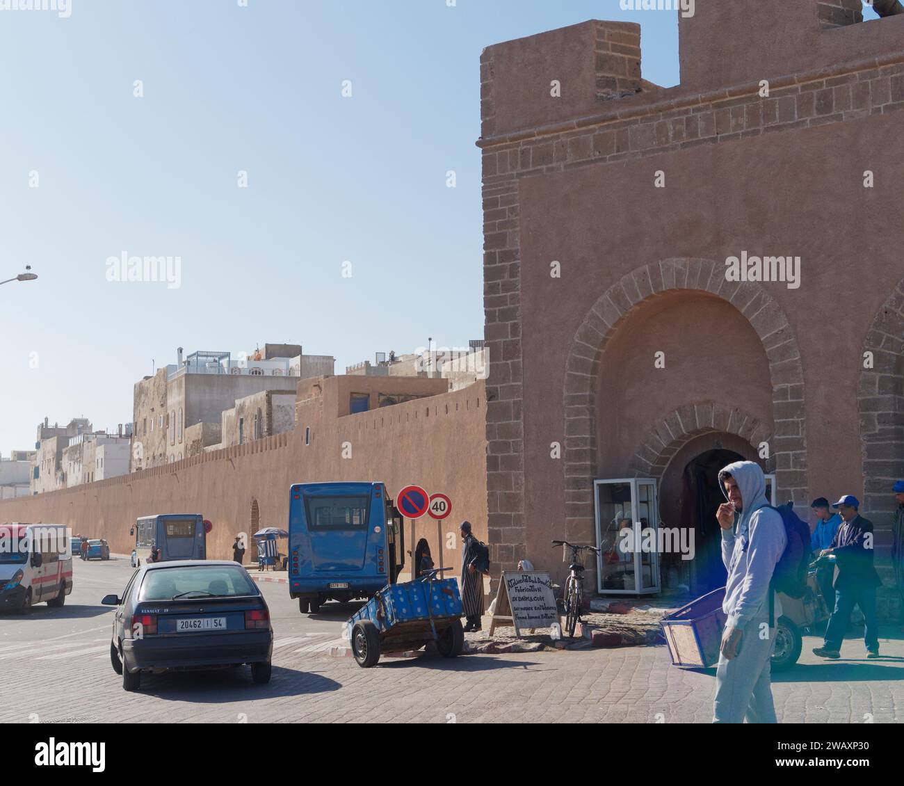 Mura della città e medina storica esterna con auto, autobus, carretto e persone nella città di Essaouira, Marocco. 7 gennaio 2024 Foto Stock