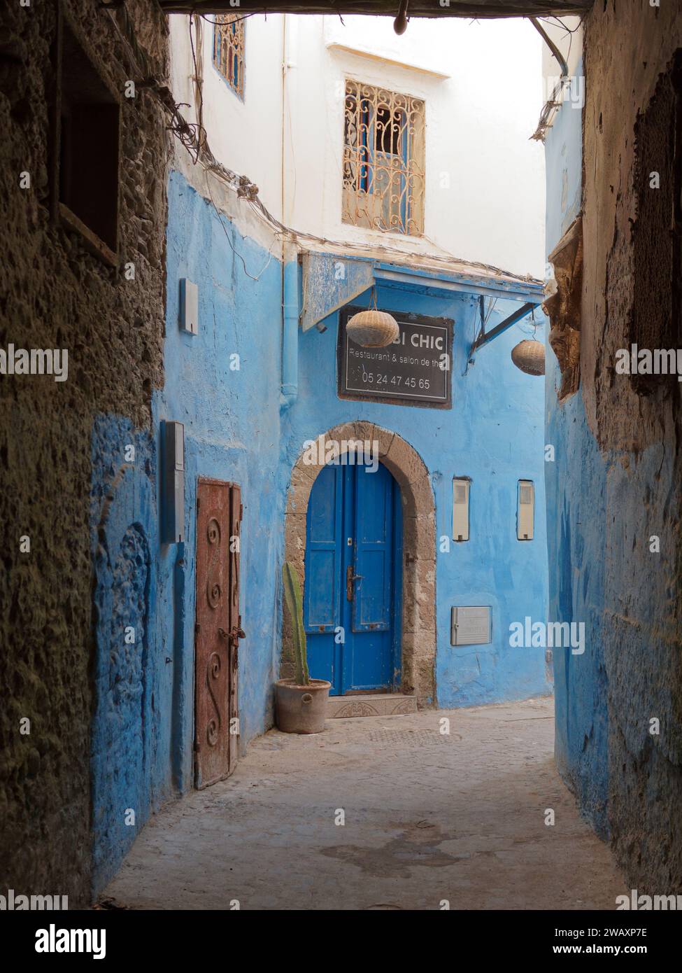 Strada piuttosto stretta con mura blu e porta nella storica medina della città di Essaouira, in Marocco. 7 gennaio 2024 Foto Stock