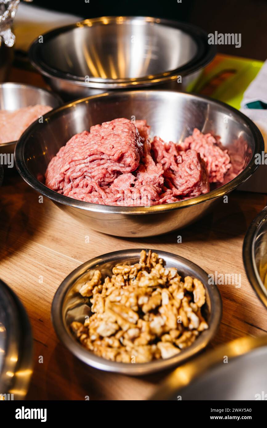 Carne macinata cruda pronta per la cottura e una ciotola di noci presentata come ingredienti su una calda superficie della cucina in legno. Foto Stock