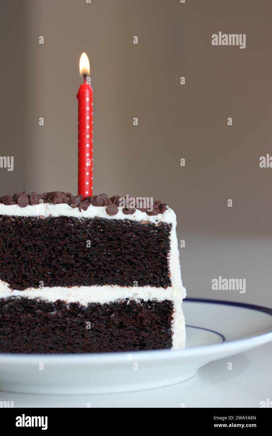 Pezzo di torta di compleanno al cioccolato con candela a pois rossa accesa Foto Stock