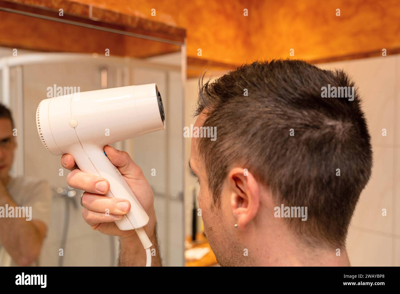 Baviera, Germania - 6 gennaio 2024: Un uomo si asciuga i capelli in un bagno con asciugacapelli *** Ein Mann föhnt sich die Haare in einem Badezimmer mit einem Föhn Foto Stock