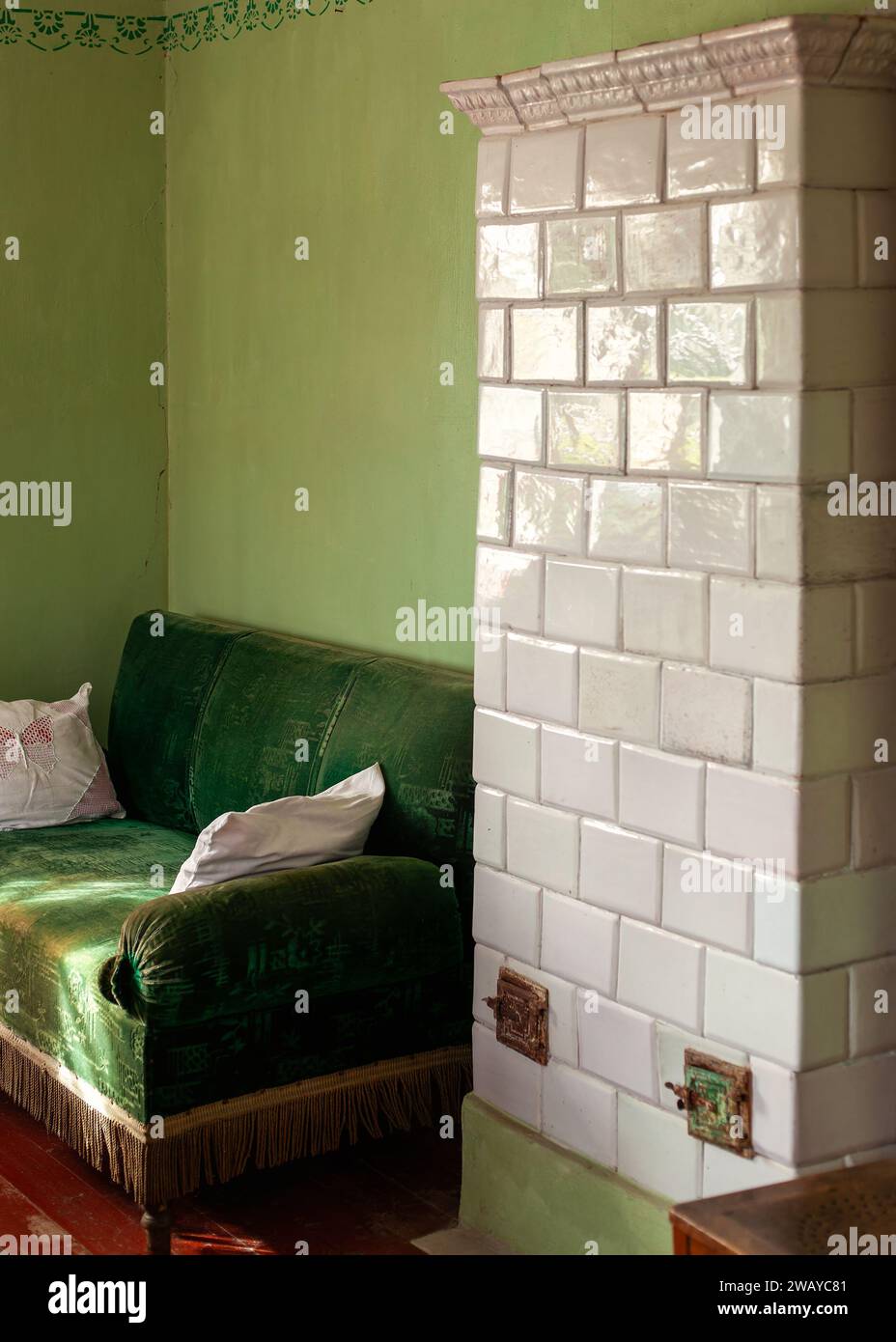 Mattoni smaltati bianchi, antiche pareti a legna e divano in velluto verde nelle vicinanze. Foto verticale di un frammento di un antico interno. Foto Stock