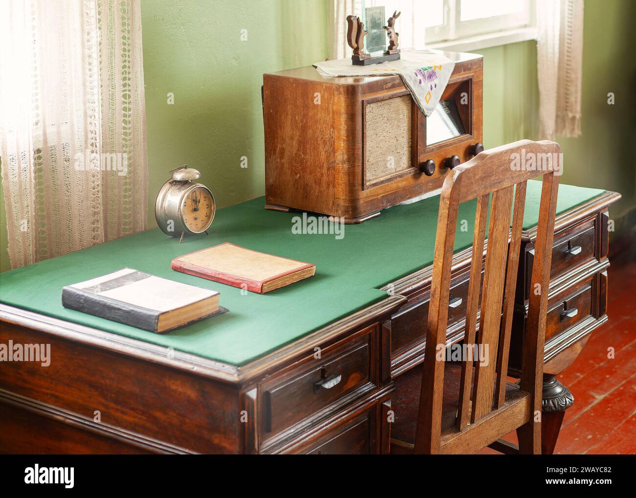 Scrivania d'epoca in materiale verde, con finestra illuminata da molti cassetti, vecchia radio e orologio. Foto Stock