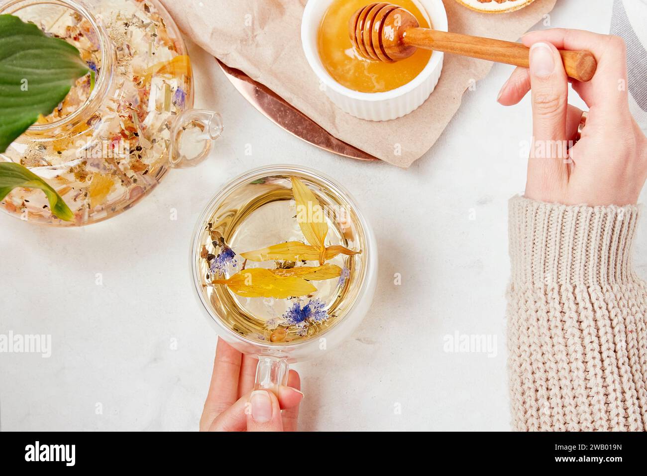 Le mani delle donne aggiungono miele alla tazza da tè. Stile di vita sano del tè alle erbe di montagna. Concetto di erbe disintossicanti Foto Stock